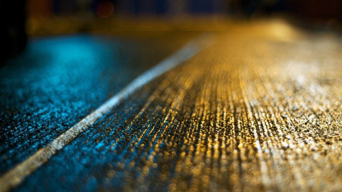 Wet road at night with street markings and reflections of yellow and blue lights