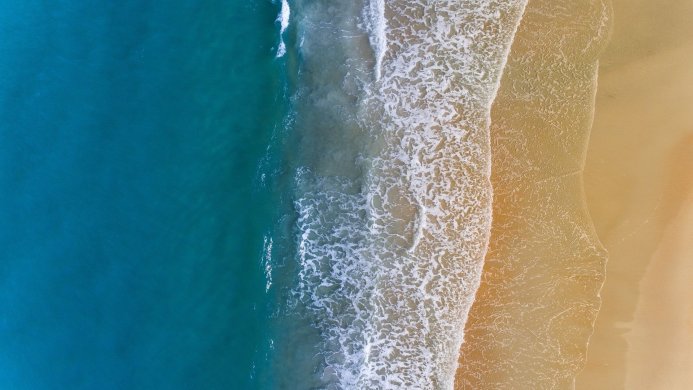 Aerial view of waves crashing on a sandy beach, showing the meeting of blue water and beige sand