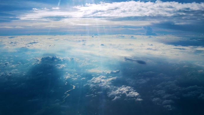 An aerial view of fluffy white clouds against a clear blue sky with sun rays