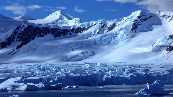 Antarctic landscape with icebergs and mountains covered in snow under a blue sky