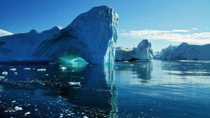 Large iceberg with an archway reflecting in the arctic waters of the ocean on a sunny day