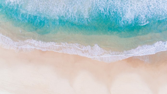 Aerial view of a beach with blue water and beige sand