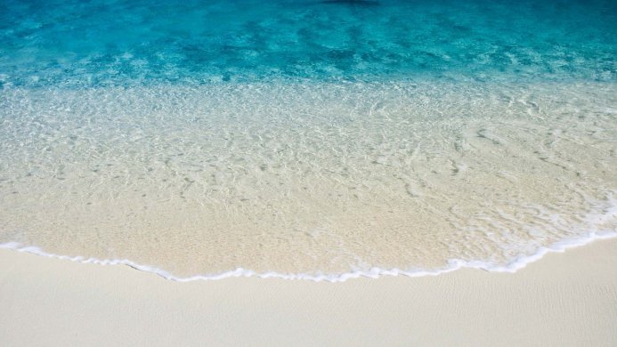 Beach with clear water and white sand. Blue water meets the shore