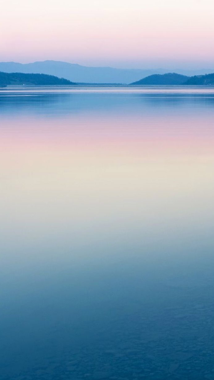 Calm lake with mountains in the distance, pastel sky