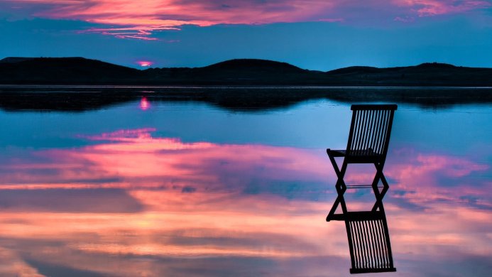 Chair in lake reflecting sunset colors, peaceful scene