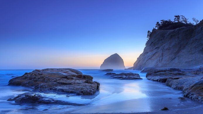 Coastal landscape with a sea stack, rocks, and long exposure of ocean water, in shades of blue and gray