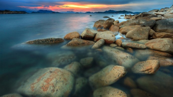 Coastal scene with rocks in water during sunset