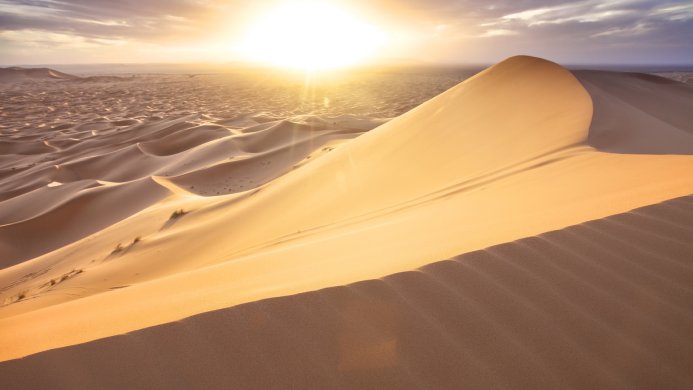 Sand dunes in a desert landscape with a bright sunrise or sunset