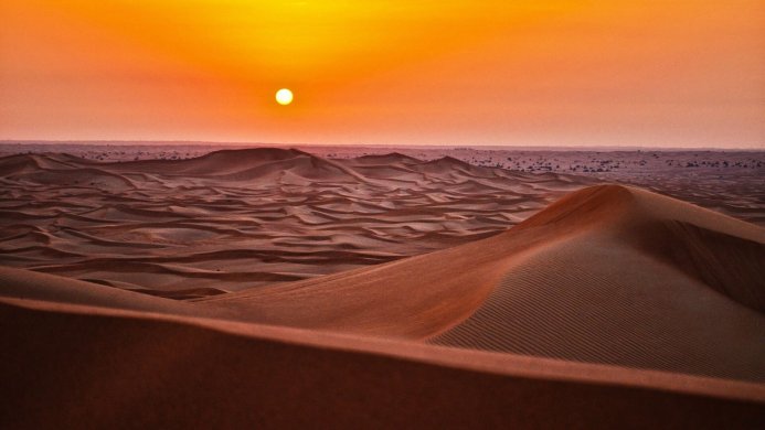 Desert landscape with rolling sand dunes under a sunset sky