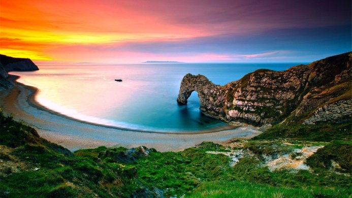 Durdle Door rock arch on a beach at sunrise with vibrant colors