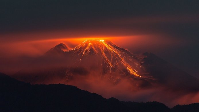 Erupting volcano with lava flowing down its slopes against a dark sky