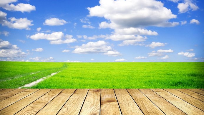 Green field under a blue sky with white clouds, and a wooden deck in the foreground