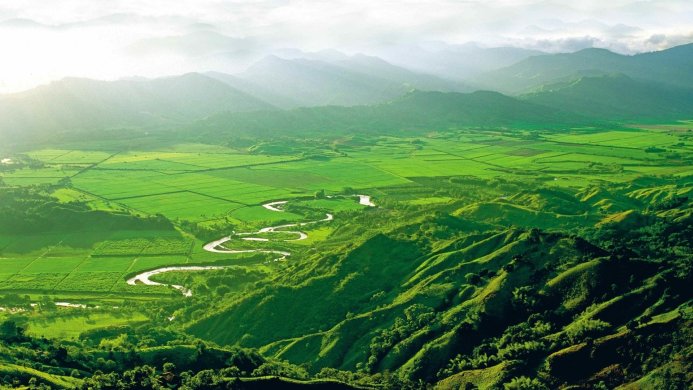 Lush green valley with a winding river and distant hills, aerial view