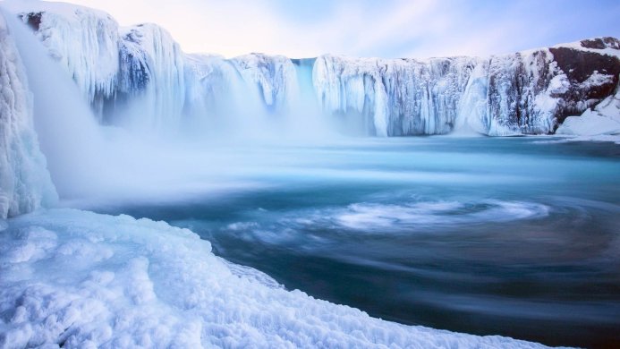 Icy waterfall with snow and frozen water formations, turquoise water below