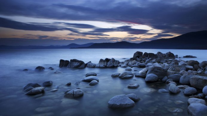 Rocks in a calm lake during twilight with a mountain range in the background