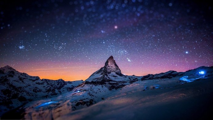 Matterhorn mountain at night with a starry sky and snow-covered landscape