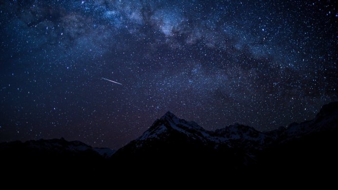 Milky Way over snow-capped mountains with a meteor streaking across the dark blue starry sky