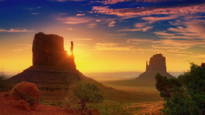 Monument Valley buttes at sunset with sun rays shining between the rock formations