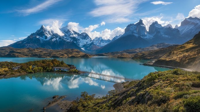 Mountain range reflecting in a lake with a bridge and buildings