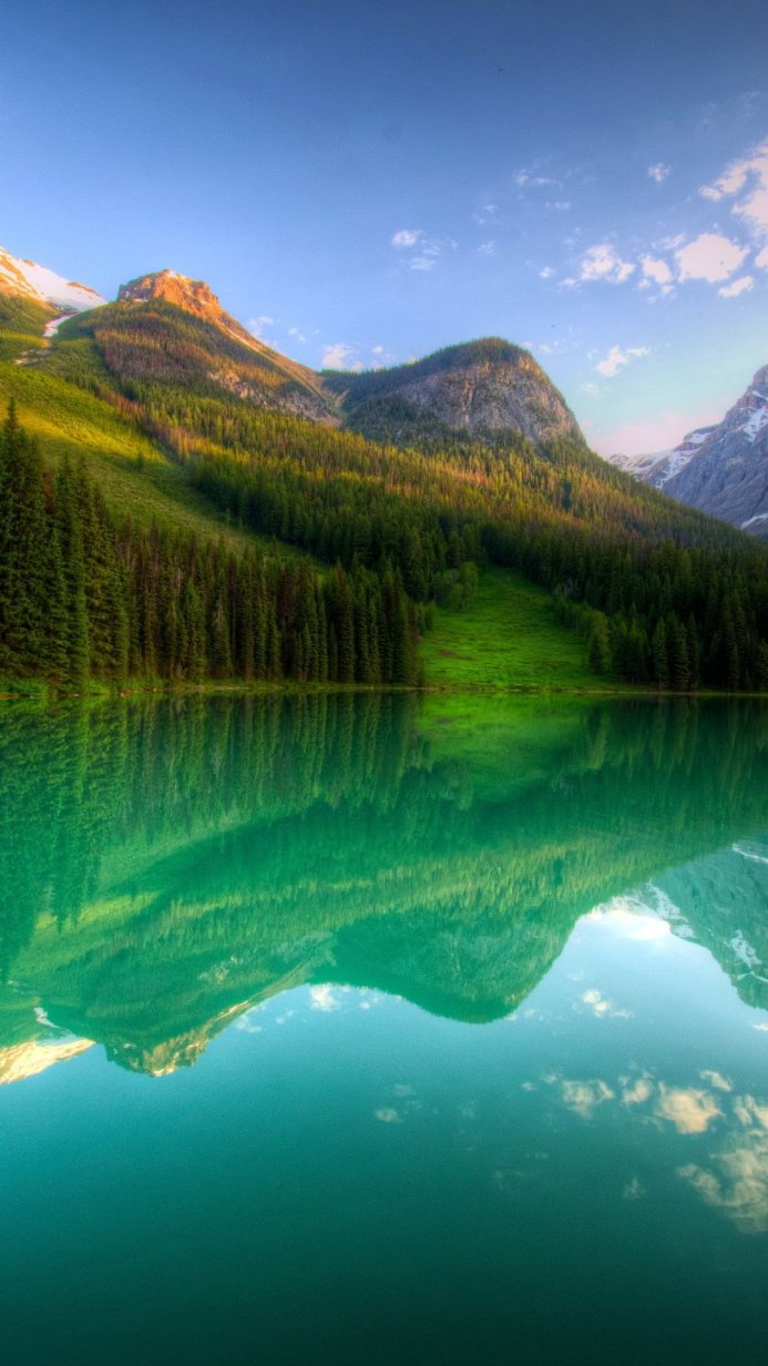 Mountain range reflecting in a teal lake surrounded by a green forest