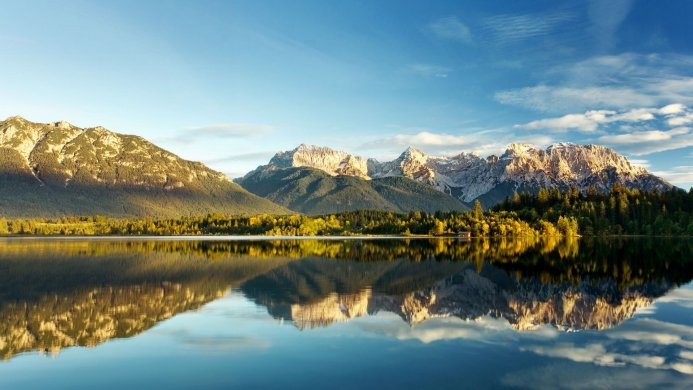 Mountain range reflecting in a calm lake surrounded by trees on a sunny day