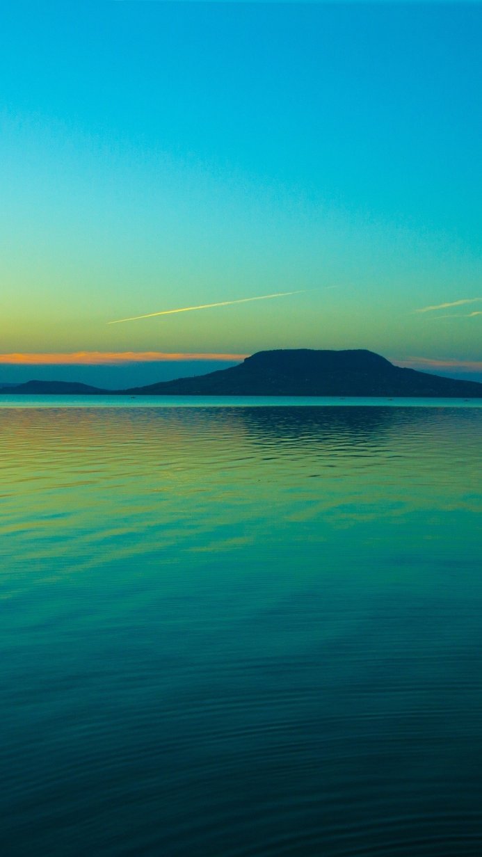 A mountain range across a serene body of water at sunset with blue and green tones in the sky and water