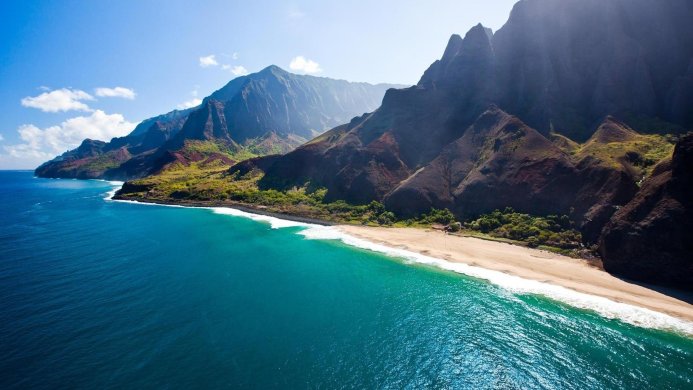 A scenic view of mountains meeting the sea on a sunny day