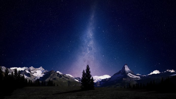 Mountains and trees under a starry night sky with the Milky Way stretching overhead