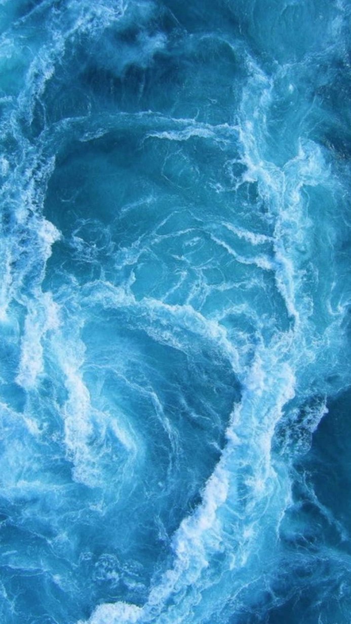 Aerial view of ocean water with foamy waves, blue and white colors