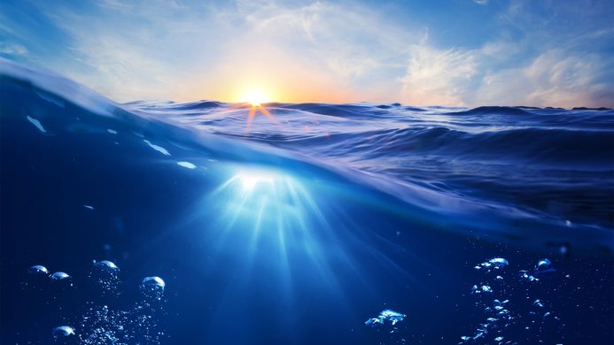 Underwater view of ocean waves at sunset with sun rays and air bubbles