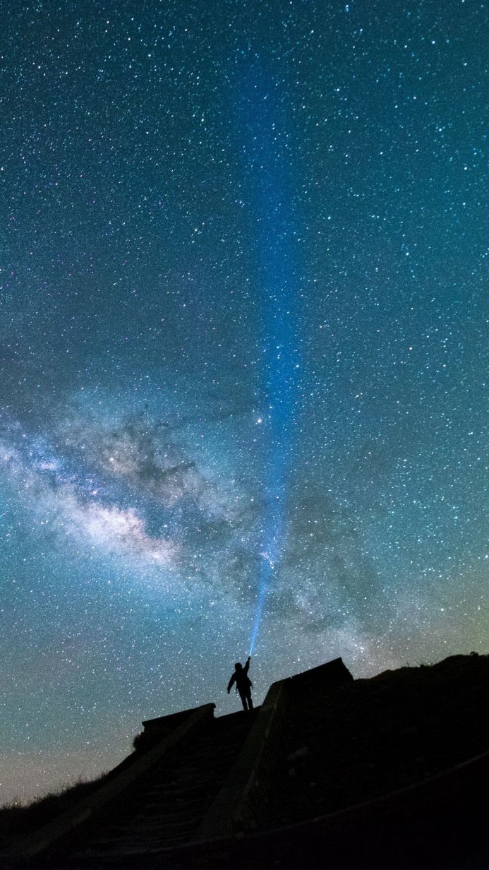 Silhouette of a person pointing a light towards the starry sky and the Milky Way