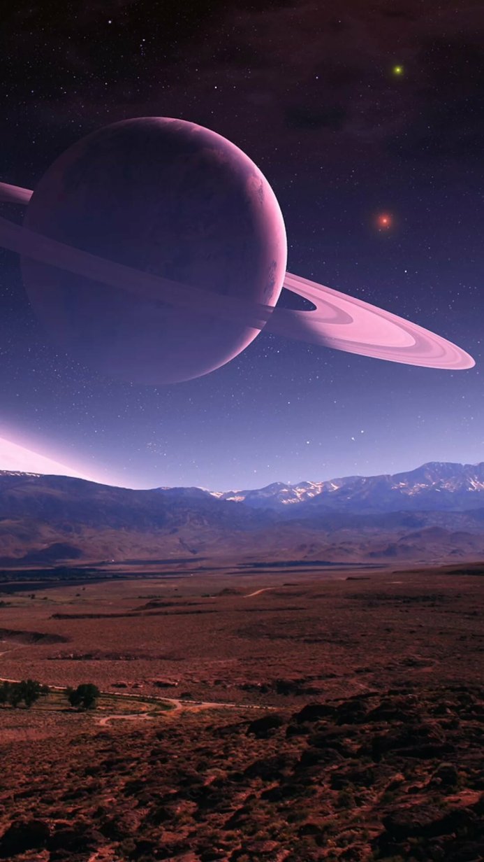 A pink Saturn above a landscape of mountains under a starry sky