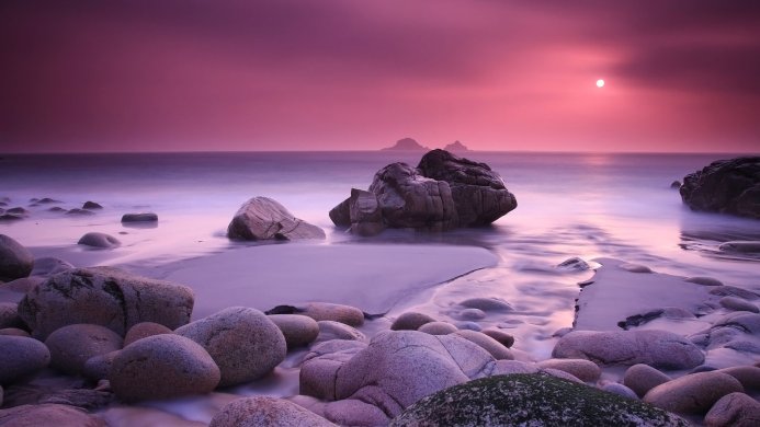 Rocks on a beach at sunset with purple sky and water