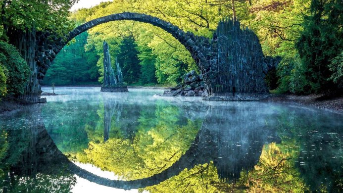 The Rakotz Bridge reflected in water creating a full circle surrounded by green trees