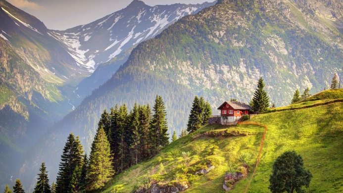 Red house on a green hillside with mountains in the background