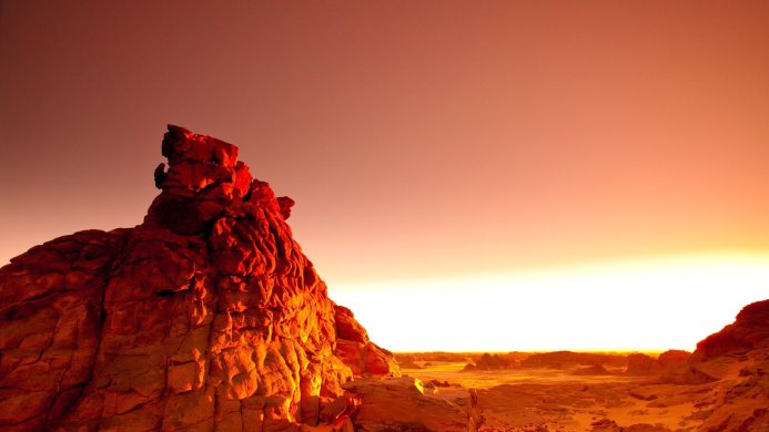 A red rock formation in a desert landscape under a sunset sky