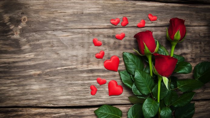 Three red roses and small red hearts on a wooden surface