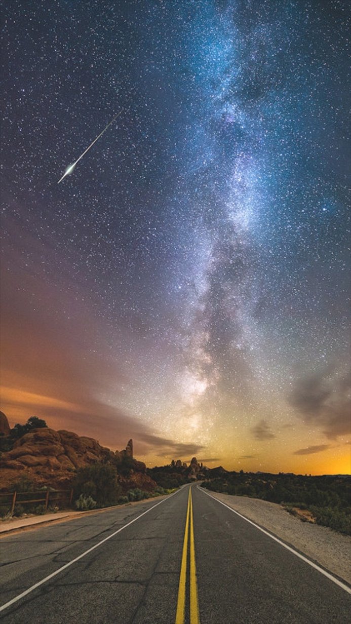 Road leading under the Milky Way at night with a visible meteor