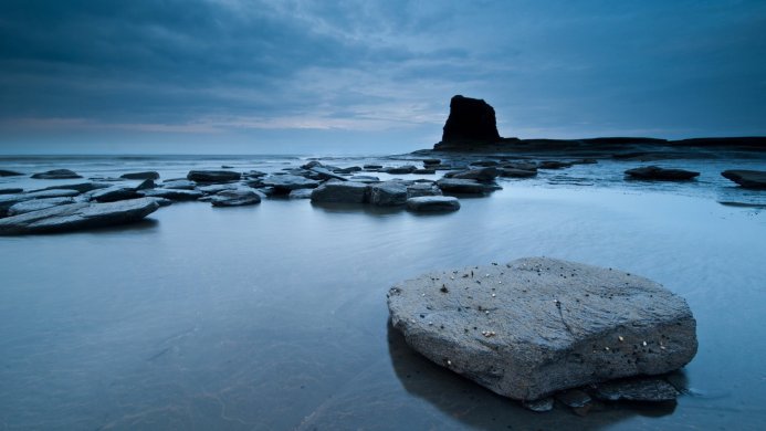 Rocks and sea stack on a beach under a cloudy blue sky