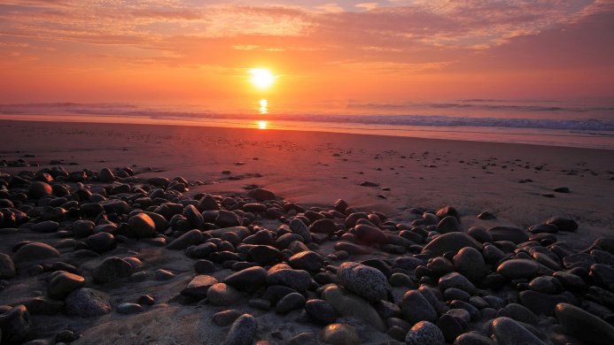 A rocky beach at sunrise with orange sky and ocean waves