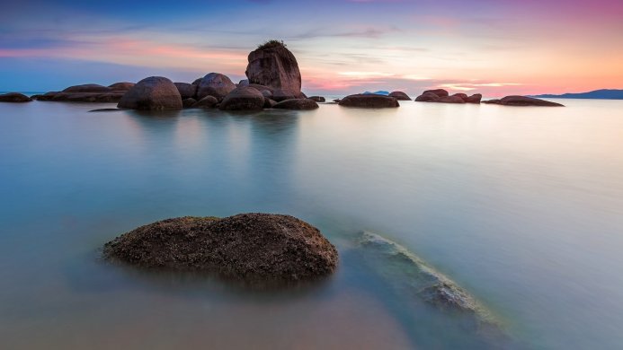 Seascape with rocks in the foreground and pastel sunset sky reflected in the water