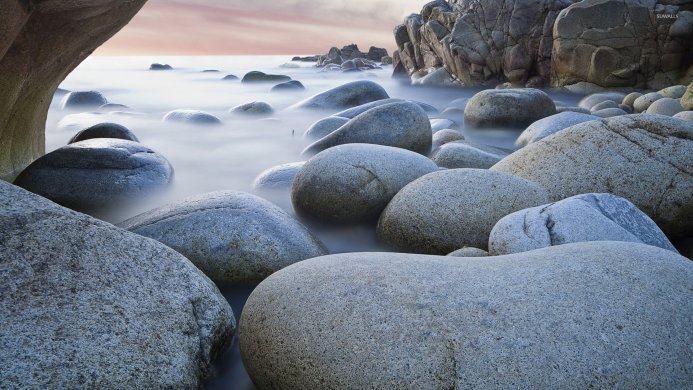 Large rocks in the water along a misty shore, with other rocks and sky in the background