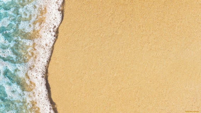 A sandy beach with sea foam and turquoise water lapping at the shore