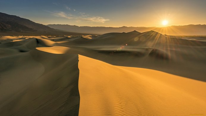 Sand dunes in the desert at sunset with mountains in the background