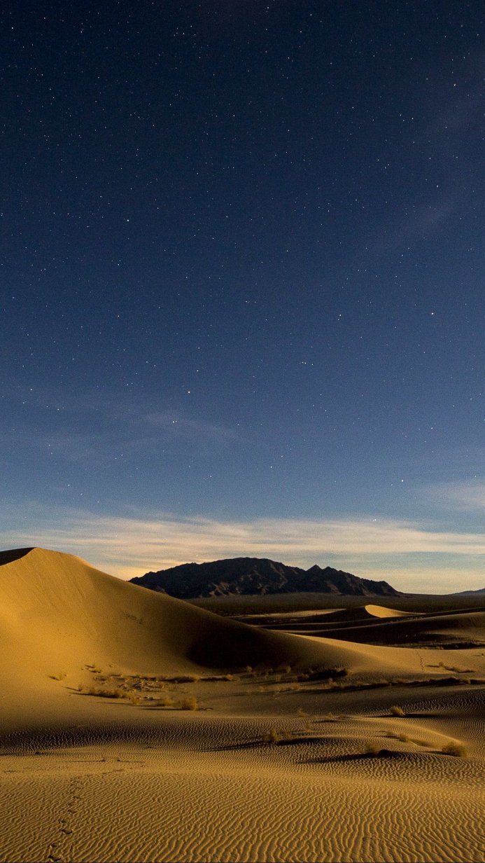 Sand dunes under a starry night sky, with mountains in the distance