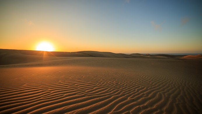 Sand dunes at sunset with a clear blue sky overhead