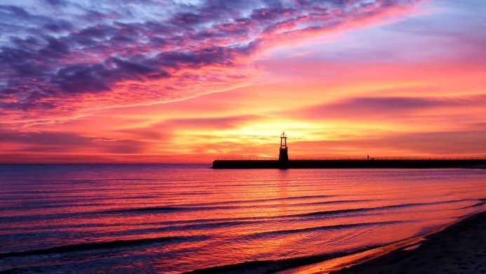 Colorful sunset over a sea with a lighthouse on a pier