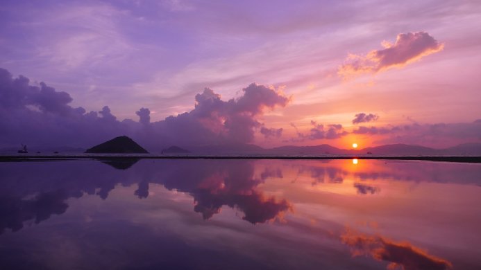 A serene sunset reflecting in shallow water, with an island in the distance