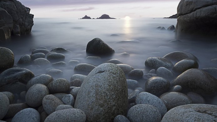 Smooth rocks in the sea, with islands and sun in the background