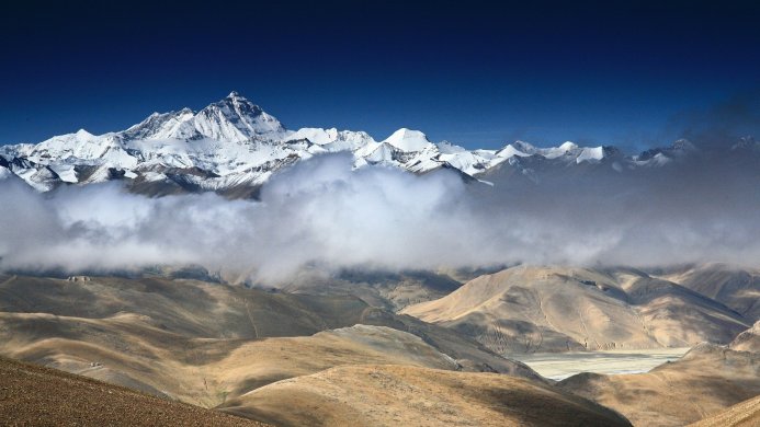 Panoramic view of snow-capped mountains partially obscured by clouds under a blue sky